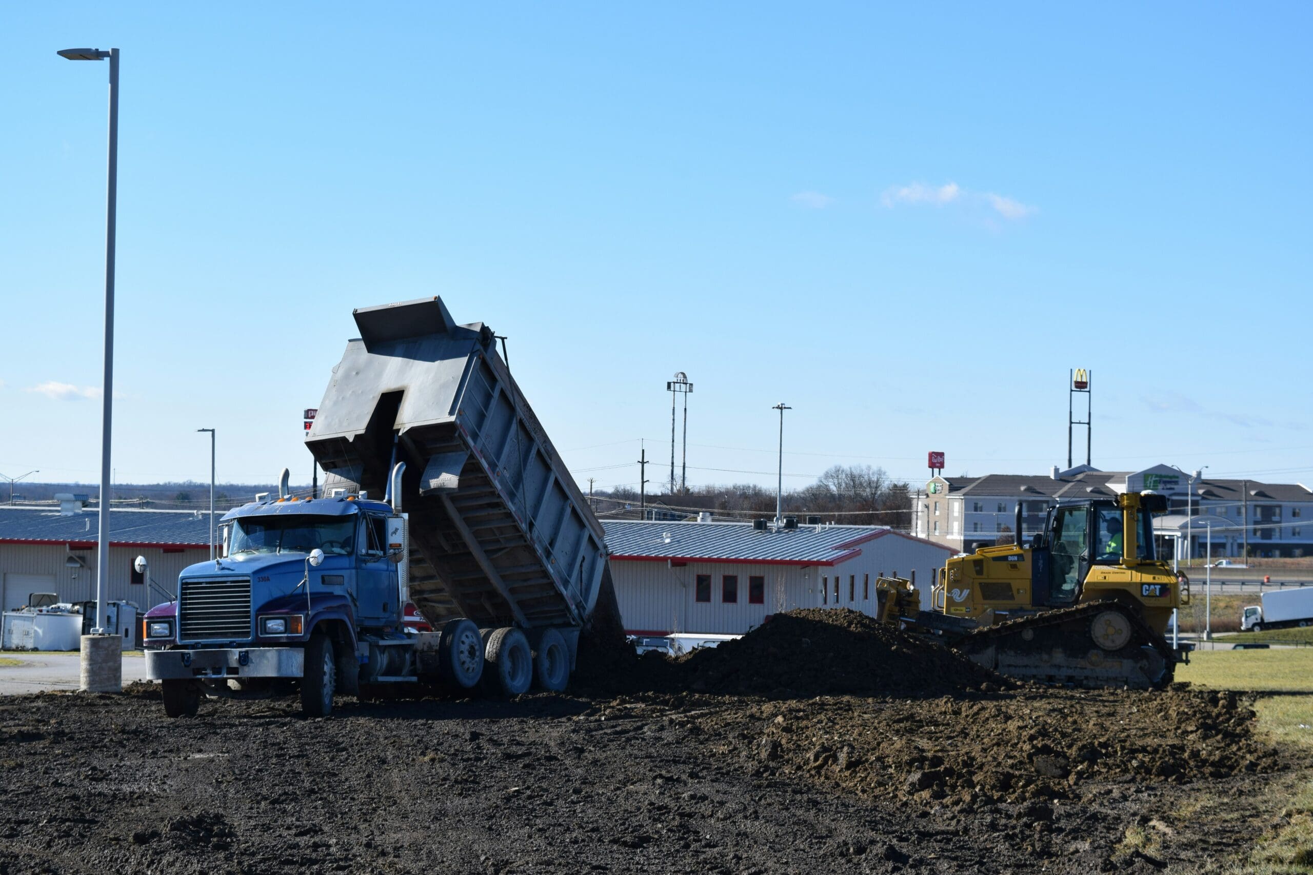 Dump truck unloading soil while bulldozer spreads fill material for commercial site development and grading.