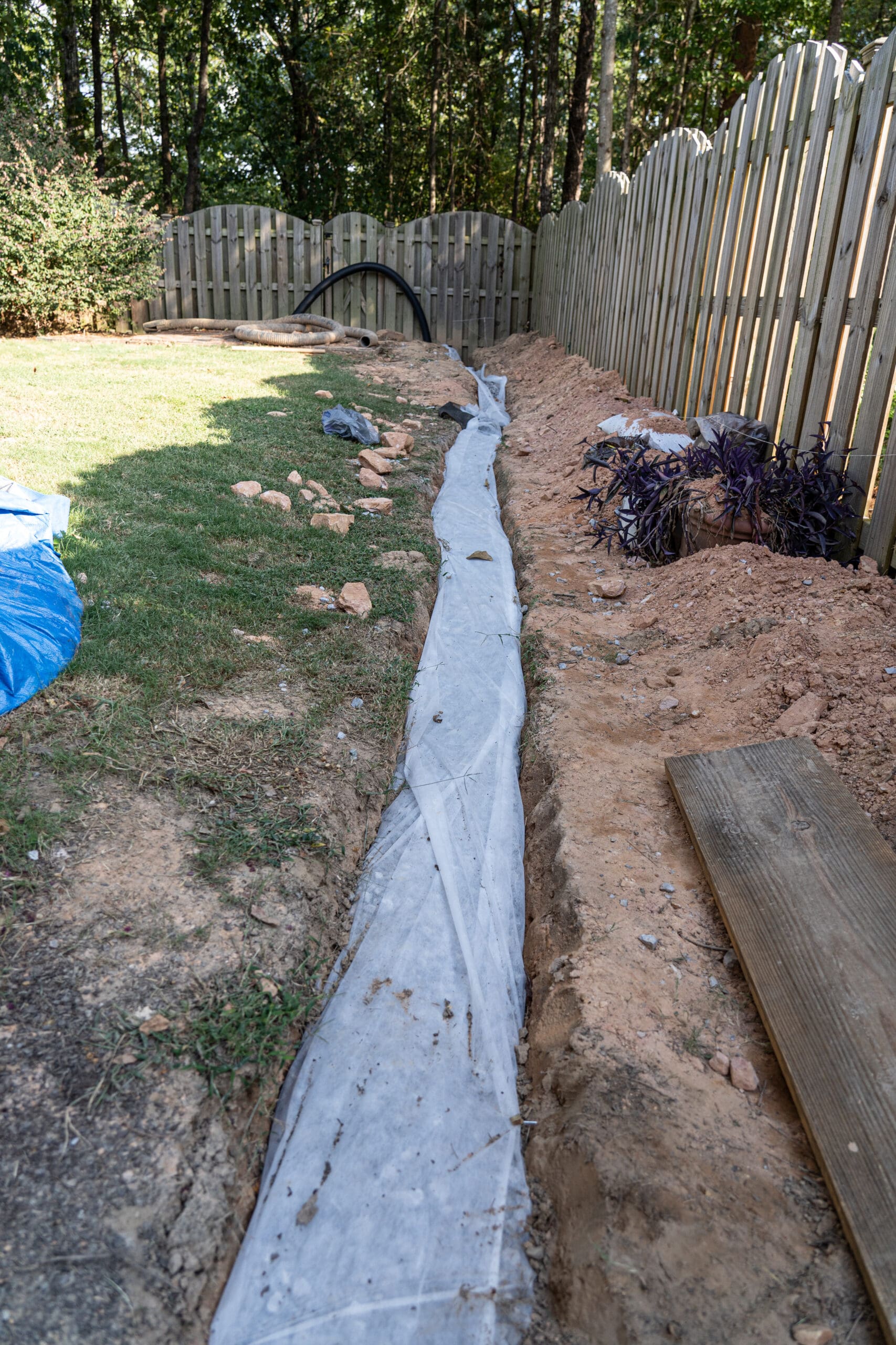 French drain system installation in residential yard with gravel trench and drainage fabric for proper stormwater management.