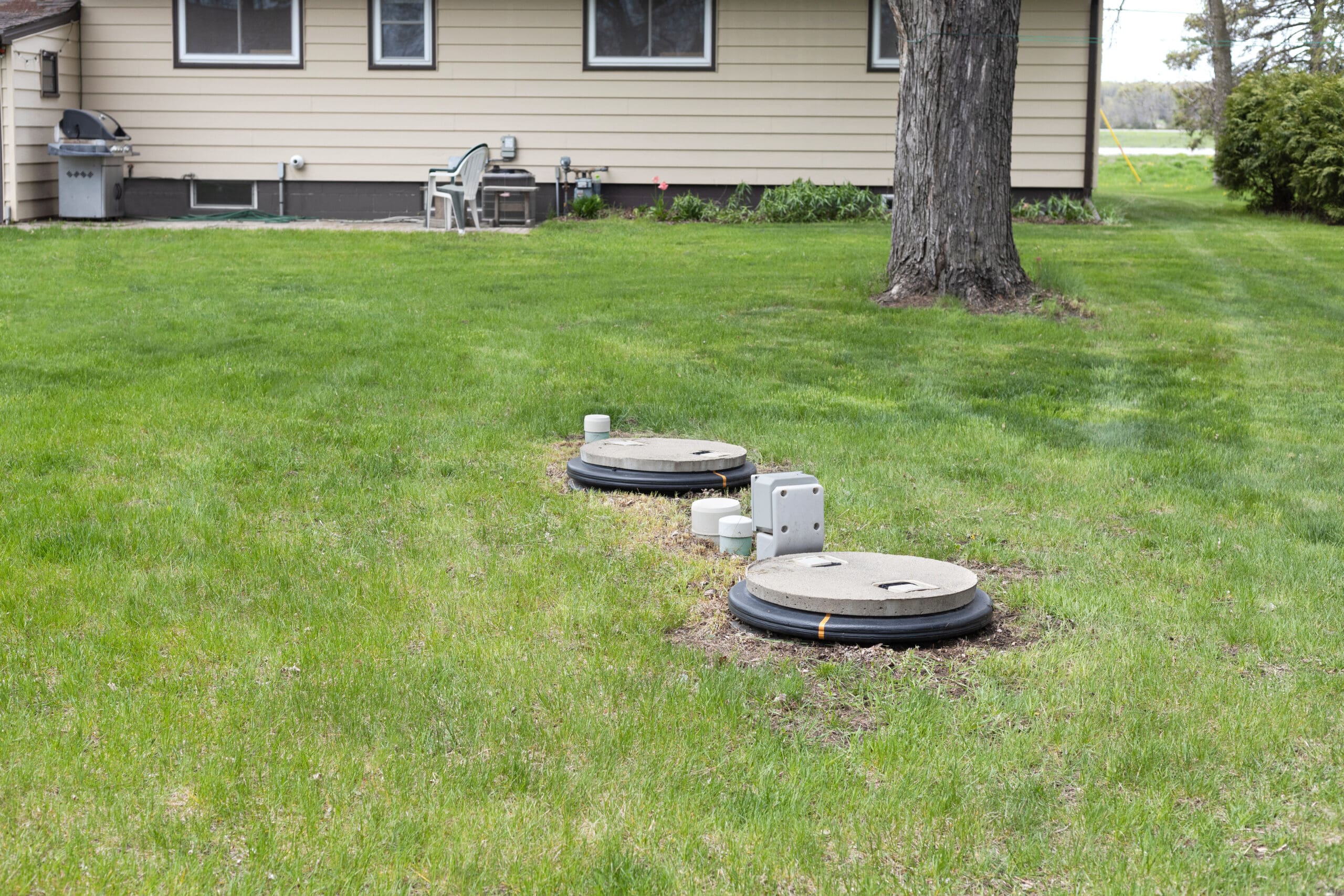 Residential septic system installation with dual tank lids in backyard lawn near home.
